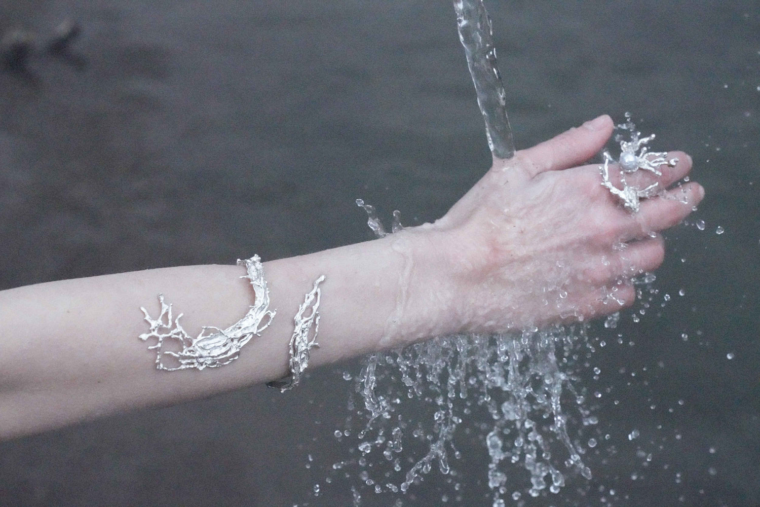 Hand with silver bracelets touching water on a beach
